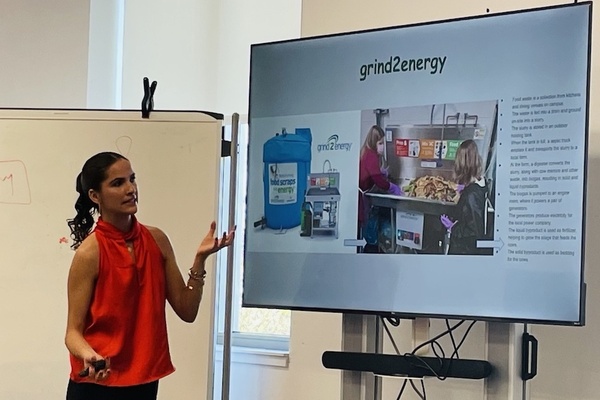 Claudia Interiano gestures toward a TV screen with a picture of the Grind2Energy system during her presentation at the IDEA Center