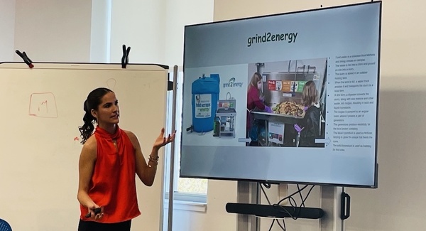 Claudia Interiano gestures toward a TV screen with a picture of the Grind2Energy system during her presentation at the IDEA Center